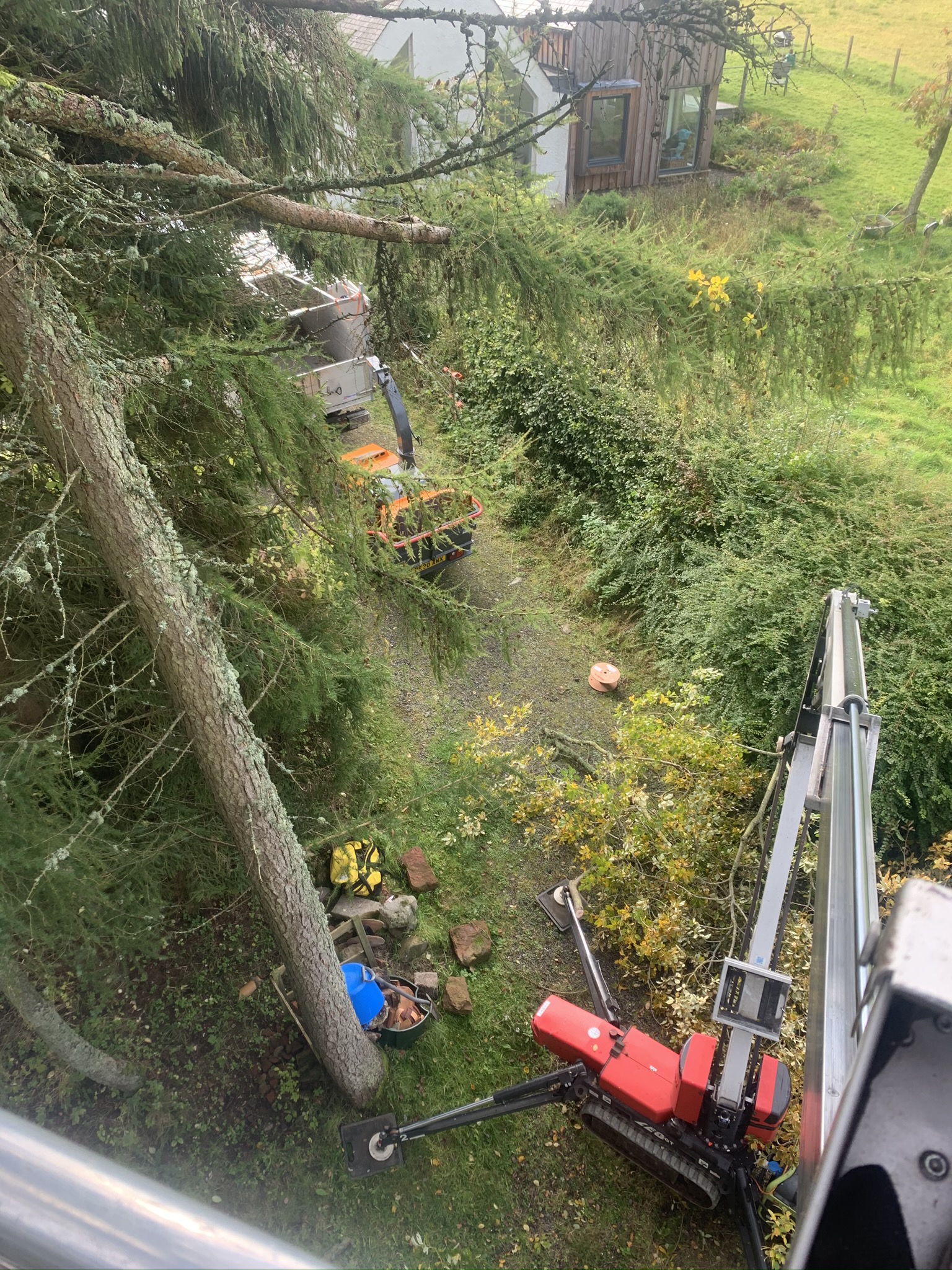 Gallery #2 An overhead view from a tracked aerial platform showing tree work equipment and cut branches beside a wooden house.