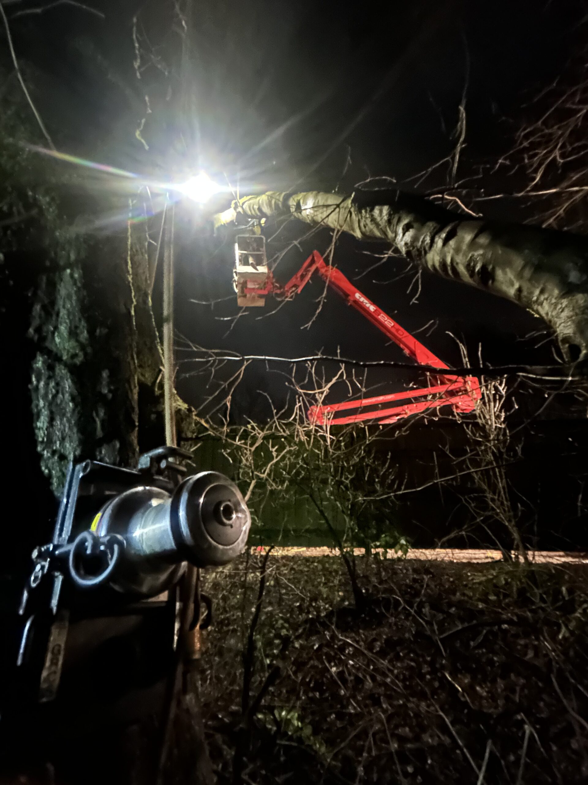 An aerial work platform being used to access a storm-damaged tree during night-time emergency tree work.