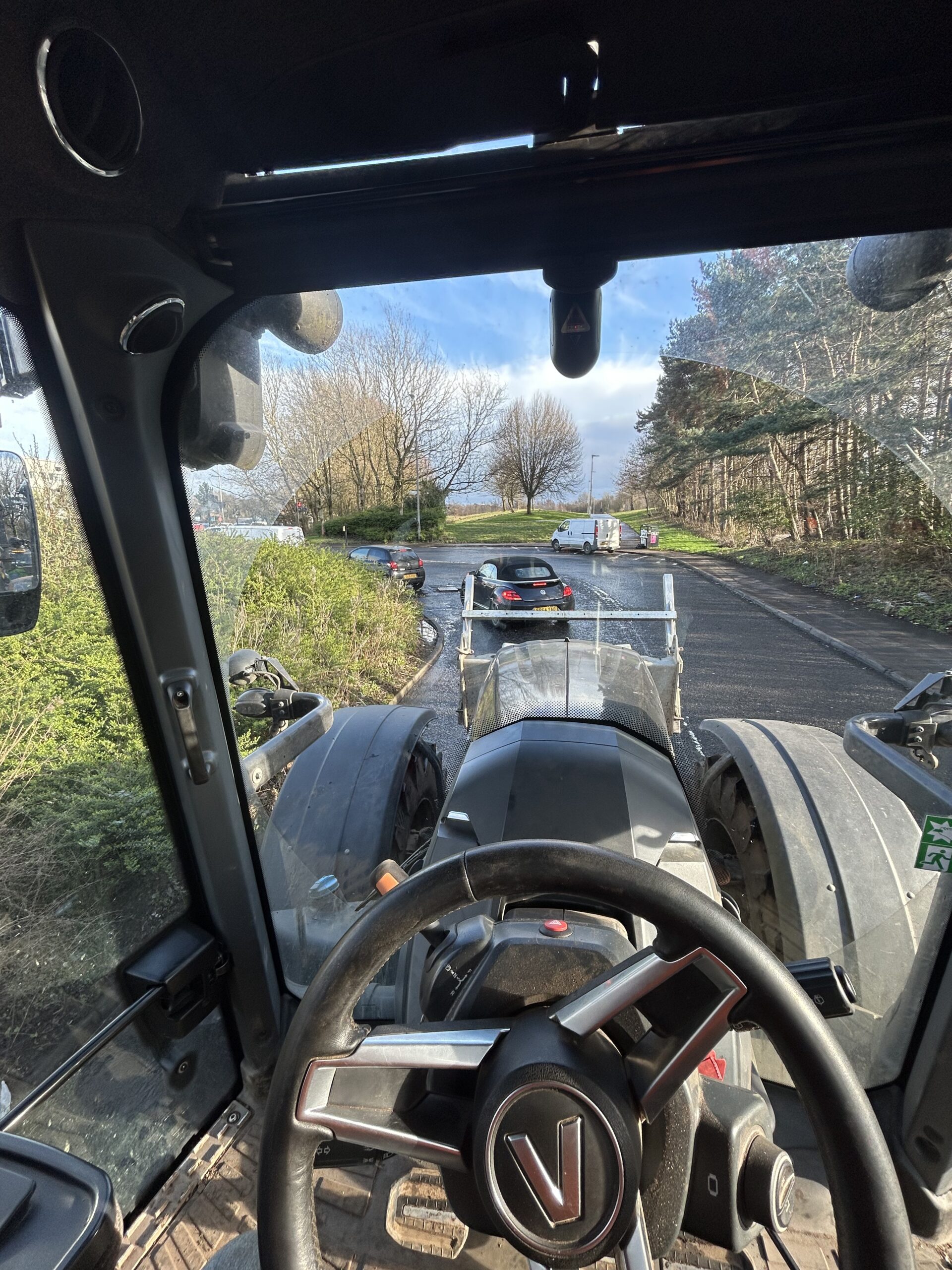 Gallery #46 View from inside a tractor cab towing a trailer loaded with a car through a car park.
